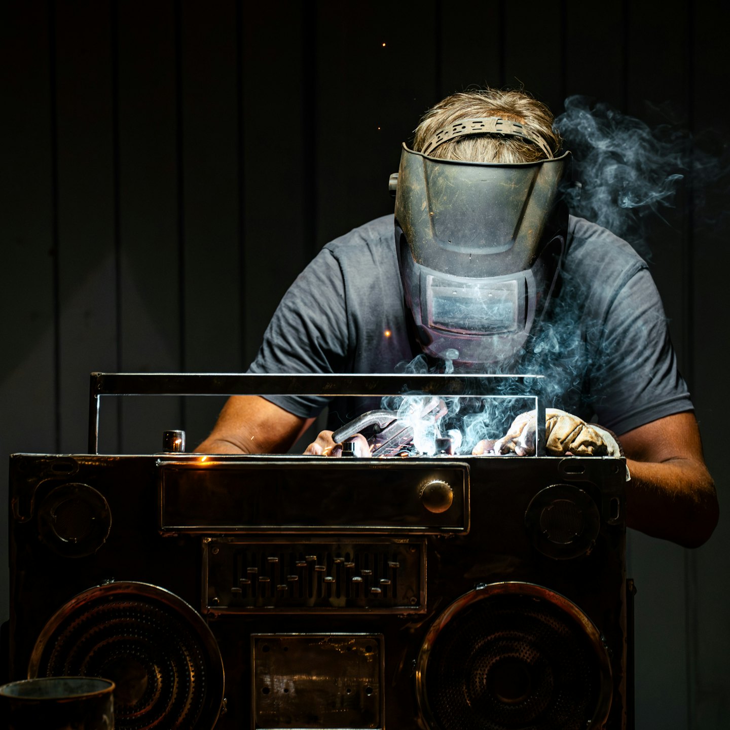 Spawacz w masce i rękawicach tworzy metalową konstrukcję boomboxu.