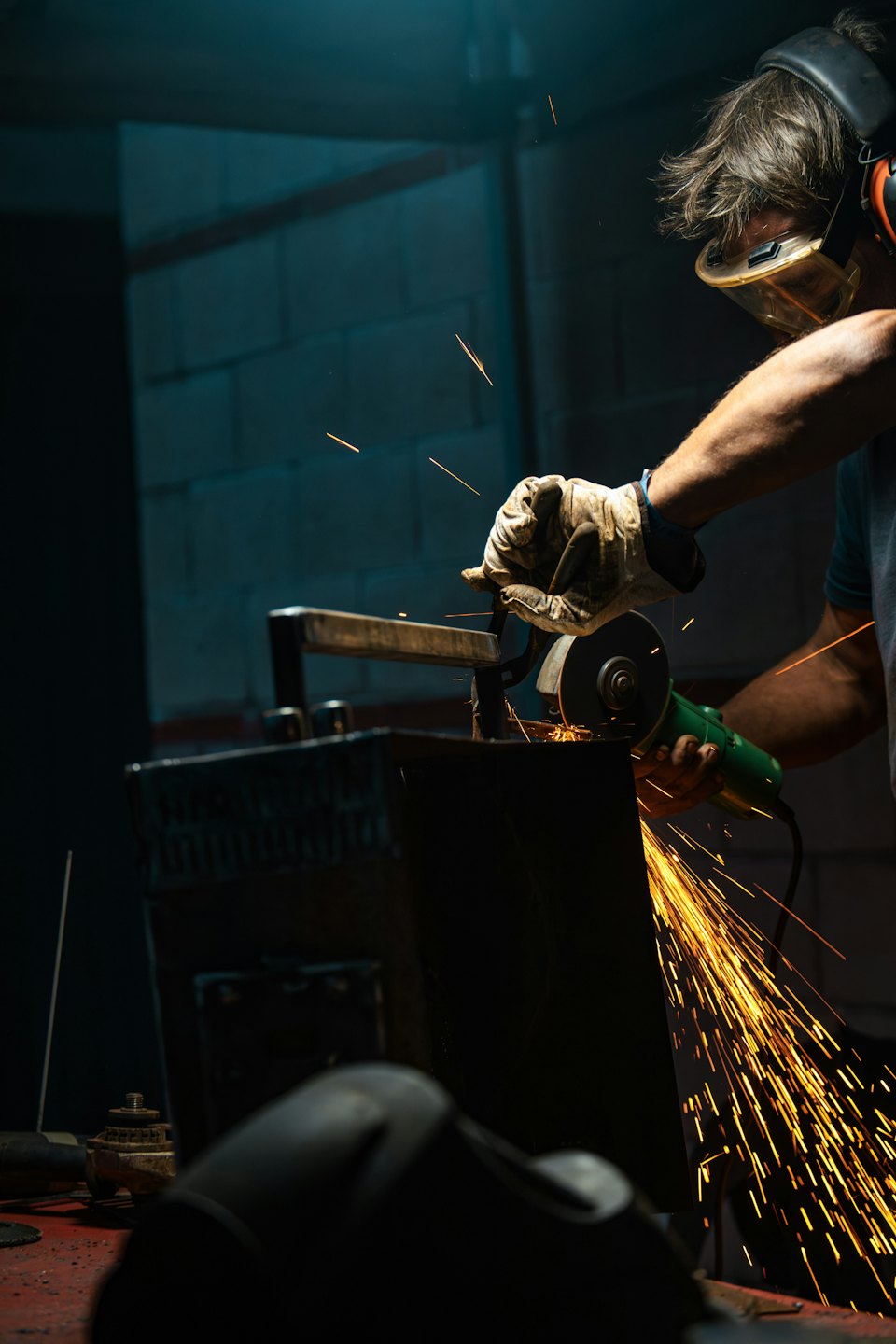 Pracownik w nausznikach szlifuje metal, sypiąc iskrami.